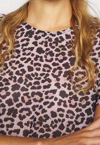Camiseta rosa claro con un diseño de estampado de leopardo negro. Tejido suave con cuello redondo y mangas cortas, mostrando un patrón texturizado.