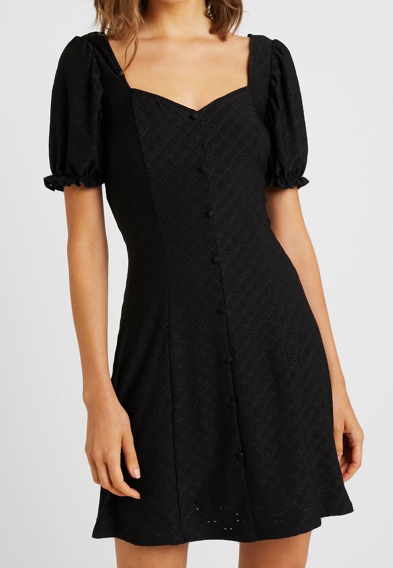 Svart klänning med puffärm, fyrkantig halsringning, strukturerad tyg med diamantmönster och knäppning fram.