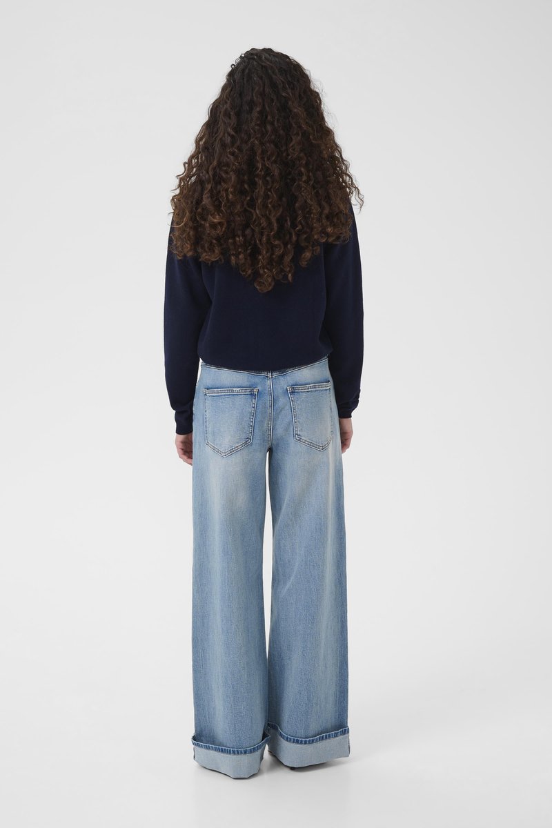 Jean large coupe ample bleu clair avec une texture délavée, comprenant des poches arrière et des ourlets retroussés, associé à un haut à manches longues bleu foncé.