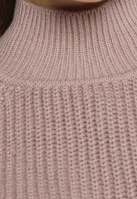 Pull en maille côtelée rose clair avec un col haut orné d'un motif texturé et un tissu doux. Zoom sur l'encolure et le tissu supérieur.