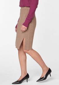 Beige Strickrock in knielanger Form mit seitlichem Schlitz, kombiniert mit schwarzen spitzen Absatzschuhen. Die Textur wirkt weich und fein gestrickt.
