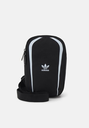 Borsa a tracolla nera Adidas con tracolla regolabile, strisce laterali bianche e tasca frontale con zip su sfondo semplice.