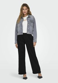 Jachetă din denim de culoare bleu deschis, cu nasturi tip capse și două buzunare pe piept, asortată cu un tricou alb și pantaloni negri cu croială largă. Pantofi gri slip-on.
