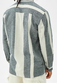 Blauw-wit gestreepte lange mouwen shirt, gemaakt van gestructureerde stof. Bevat een knoopmanchet en kraag, met gedurfde verticale strepen.