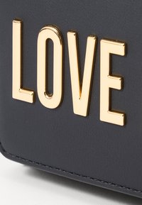 A fekete műbőr felületen kiemelkedő arany "LOVE" felirat található, sima textúrával és finom varrással a széleken.