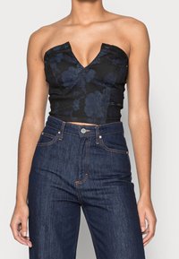 Top corto nero con motivo floreale, scollatura a V profonda, design strutturato e spalline regolabili, abbinato a jeans in denim scuri a vita alta.