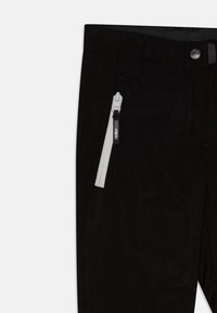 Mustad mustreeritud taskudega mustad püksid, millel on valge lukk. Materjal näeb välja vastupidav ja sileda tekstuuriga. Rõhutuseks on bränditud riistvara detail.