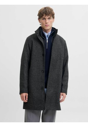 Donkergrijze wollen blendjas met een gestructureerde afwerking, knoopsluiting aan de voorkant en hoge kraag. Gemaakt over een marineblauwe laag, getoond tegen een neutrale achtergrond.