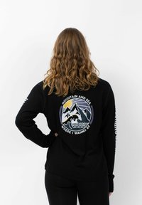 Zwarte langemouwen shirt met een geborduurde graphic van een berg en zee op de achterkant, met de tekst "BERG EN ZEE WAAR IK WIL ZIJN."