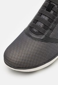 Schwarzer Mesh-Sneaker mit strukturiertem Muster, verstärktem Fersenbereich und flachen Schnürsenkeln, ausgestattet mit einer kontrastierenden weißen Sohle und glatten Akzenten.