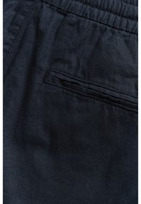 Tissu bleu marine foncé avec une poche horizontale à fente et des coutures visibles, doté d'une ceinture élastique sur le bord supérieur.