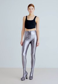 Musta lyhyt toppi, metallinväriset hopeiset legginsit, istuva malli, korkea vyötärö. Mallilla on yllään korkean koronkengät nilkkamittaisena; sileä, kiiltävä pinta.