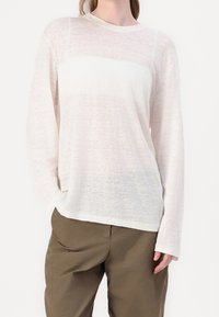 Haut blanc à manches longues en tissu léger avec une texture transparente et une coupe légèrement ample. Associé à un pantalon ample vert olive.