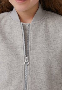 Veste bomber grise en tissu feutré, dotée d'une fermeture éclair argentée et d'un col côtelé assorti. La vue en gros plan met en évidence la texture et les détails.