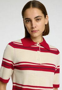 Gebreid polo-shirt met rode en marineblauwe strepen op een crèmekleurige achtergrond, met een rode kraag en een drieknopenlijst. Korte mouwen.