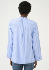 Camicia a righe blu e bianche con maniche lunghe, dettaglio di legatura sul retro, orlo arrotondato e polsini larghi, realizzata in tessuto leggero.