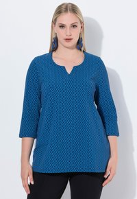 Top azul con patrón de espiga, con escote en V y mangas de tres cuartos, hecho de una tela suave, combinado con pantalones negros.