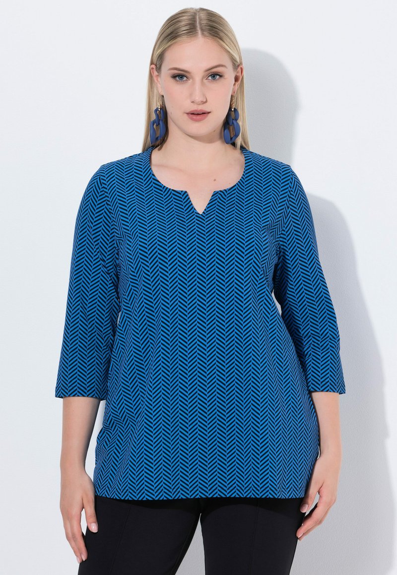 Top azul con patrón de espiga, con escote en V y mangas de tres cuartos, hecho de una tela suave, combinado con pantalones negros.