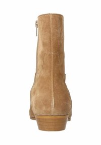Bottine en suède tan avec une fermeture éclair au dos et un petit talon en bois. Elle présente une texture lisse et un minimum de détails de couture.