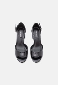 Sorte højhælede sandaler med en glansfuld lakfinish, åbent tådesign og ankelrem. Har en glat tekstur og minimalistisk design.
