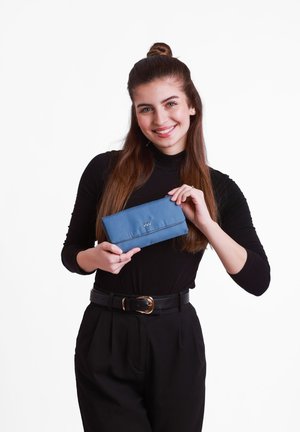 Blue fabric wallet with a simple flap design, featuring a stitched logo and a smooth texture, held by a person wearing black attire.