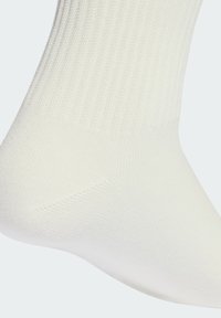 Biela bavlnená ponožka s rebrovanou textúrou, hladkým telom a spevnenou pätou. Tvar navrhnutý tak, aby kopíroval kontúry chodidla, s čistými okrajmi.