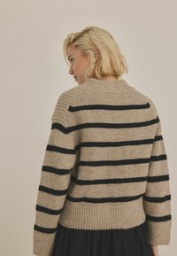 Beige stickad tröja med horisontella svarta ränder, ribbad nederkant och ärmslut, rund halsringning och mjuk textur.