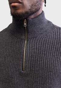 Dark gray knitted sweater with a high collar and a quarter-zip closure. Features ribbed texture and a gold zipper pull detail.
