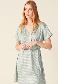 Vestido verde claro con mangas cortas, escote en V y cintura ajustada. Presenta un patrón hexagonal en toda la tela. Textura suave.