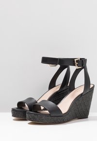 Černé wedge sandály s texturovanou tkaninou, širokými předními popruhy, nastavitelnými kotníkovými popruhy a hladkým vnitřním podšíváním.