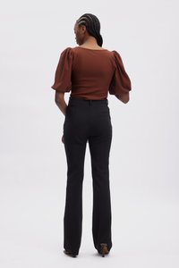 Ruda pūstų rankovių palaidinė derinama su aukštu liemeniu juodomis pritaikytomis kelnėmis. Apranga turi prigludusį siluetą ir elegantišką, minimalistinį dizainą.