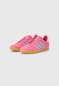 Zapatillas de ante rosa con rayas azul claro, suela de goma, cuello acolchado y un acento en el talón blanco contrastante. Diseño minimalista y superficie texturizada.