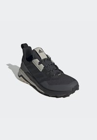 Schwarzer Sportschuh mit strukturiertem Mesh-Obermaterial, grauen Akzenten und einer robusten Gummisohle. Verfügt über ein Schnürsystem und eine Zuglasche an der Ferse.