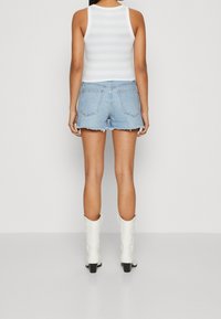 Back view of a person wearing a white striped tank top, light blue denim shorts with frayed edges, and white ankle boots.