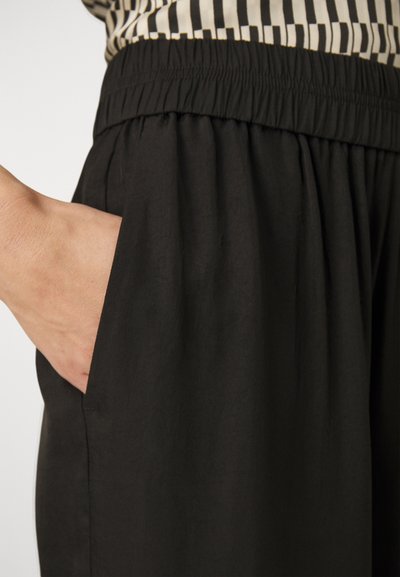 Svart bukser med elastisk midjebånd og sidelommer, med en glatt tekstur og en avslappet passform.