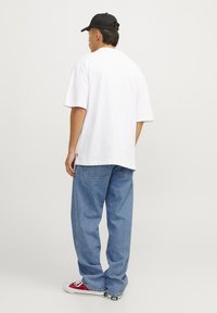 Camiseta blanca de gran tamaño, jeans sueltos azules, zapatillas rojas y blancas, y una gorra negra. Diseño sencillo, corte relajado y colores contrastantes.
