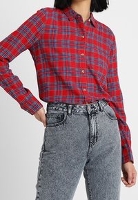 Röd och blå rutmönstrad skjorta med knappar, krage, långa ärmar och avslappnad passform, tillsammans med högmidjade, ljusgrå jeans.