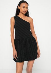 Melnas krāsas viens plecs kleita ar teksturētu audumu un pakāpienu volānu apakšu, radot strukturētu siluetu ar smalku raksta elementu.