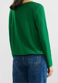 Grön långärmad topp i slätt tyg med avslappnad passform, tillsammans med blå denimjeans med bakfickor och en lätt struktur.