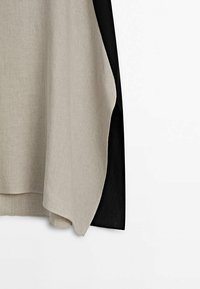 Linnen top met een beige voorkant en een zwarte achterkant, met een losse pasvorm en een gebogen zoom, die een zachte textuur en contrasterende kleuren laat zien.