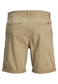 Shorts en coton beige avec poches arrière, revers roulés et une texture lisse et mate. Présente des coutures discrètes et une petite étiquette de marque en cuir.