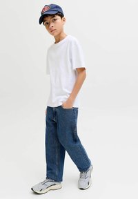 Fehér rövid ujjú póló, kék farmer egyenes szabással, szürke hálós részletekkel ellátott sportcipő, és egy tengerészkék sapka elől logóval.