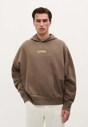 Brown oversized hoodie with a front pocket, featuring a yellow logo on the chest. Made of soft fabric with ribbed cuffs and hem.