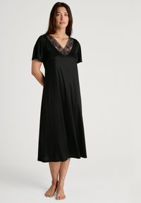 Camicetta nera con maniche corte, caratterizzata da un collo a V in pizzo e un design fluido; realizzata in tessuto morbido, che arriva a metà polpaccio.