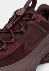 Adidași bordo cu un superior texturat, talpă din cauciuc, șireturi elastice cu ajustatori din plastic și un logo proeminent pe lateral.