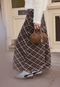 Jupe longue à carreaux marron avec des accents blancs et beiges, associée à des baskets bleu clair et un sac à main marron orné d'un porte-bonheur. Pull blanc texturé.