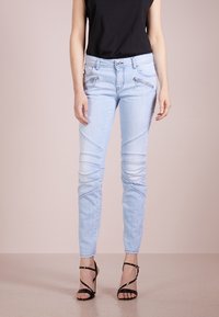 Jeans de mezclilla azul claro con un corte slim, con acentos de costura diagonal y bolsillos con cremallera. Combinados con tacones altos negros con correas.