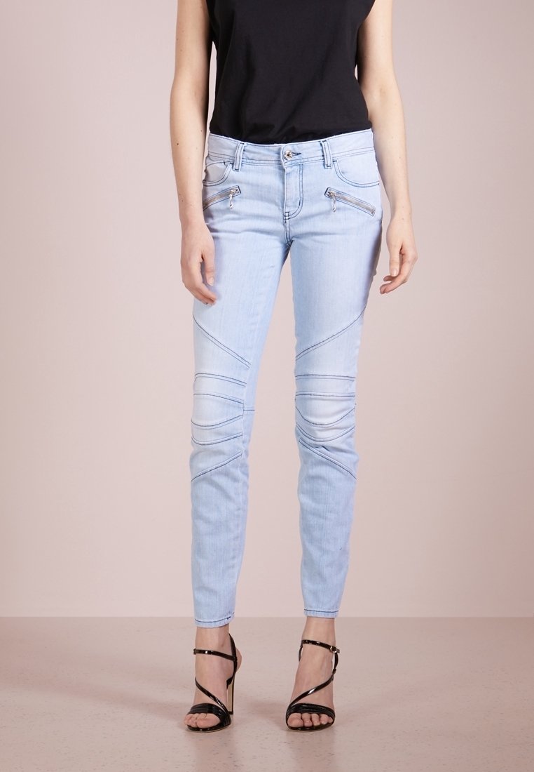 Jeans de mezclilla azul claro con un corte slim, con acentos de costura diagonal y bolsillos con cremallera. Combinados con tacones altos negros con correas.