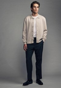 Cardigan bej deschis peste un tricou alb, asortat cu pantaloni în dungi negre și pantofi din piele negri. Textură netedă, design modern.
