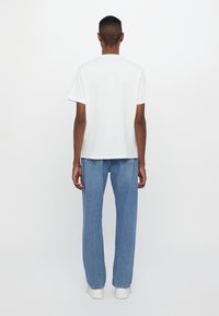 White cotton t-shirt with short sleeves, paired with light blue straight-leg jeans and white sneakers, viewed from the back.
